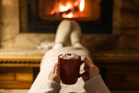 Woman with cup of hot drink resting near fireplace, closeupの写真素材