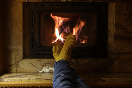 Woman in warm socks resting near fireplace indoors, closeupの写真素材