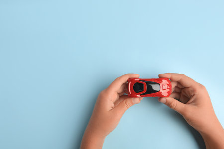 Child holding toy car on light blue background, top view. Space for text