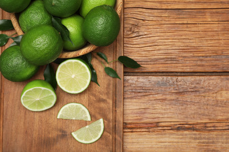 Fresh limes and green leaves on wooden table, flat lay. Space for text