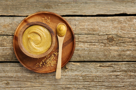 Spoon and bowl of tasty mustard sauce with dry seeds on wooden table, top view. Space for textの写真素材