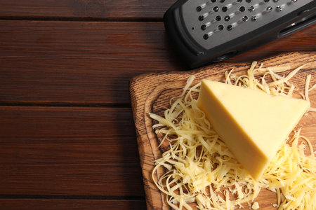 Grated, whole piece of cheese and grater on wooden table, top view. Space for textの写真素材