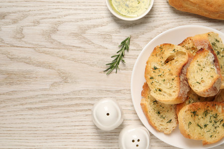 Tasty baguette with garlic, dill, rosemary and butter on white wooden table, flat lay. Space for textの写真素材
