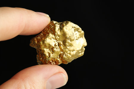 Woman holding gold nugget against black background, closeup. Space for textの写真素材