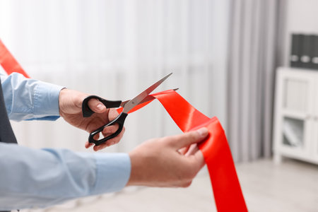 Man cutting red ribbon with scissors indoors, closeupの写真素材