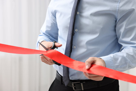 Man cutting red ribbon with scissors indoors, closeupの写真素材