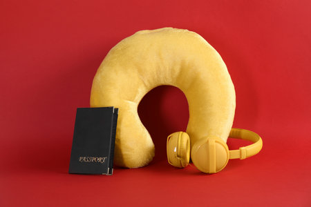 Yellow travel pillow, headphones and passport on red backgroundの写真素材