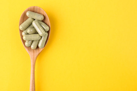 Vitamin pills in wooden spoon on yellow background, top view. Space for textの写真素材