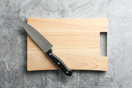 Knife and wooden board on gray textured table, top view