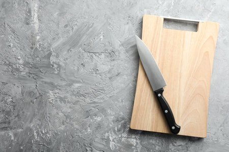 Knife and wooden board on gray textured table, top view. Space for textの写真素材
