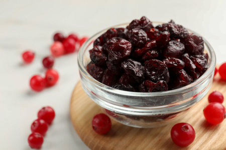 Tasty dried cranberries in bowl and fresh ones on white table, closeup. Space for textの写真素材
