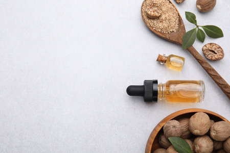 Nutmeg essential oil, nuts and leaves on light table, flat lay. Space for textの写真素材