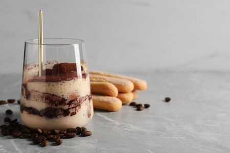 Tasty tiramisu in glass, coffee beans, spoon and biscuits on light gray table, closeup. Space for textの写真素材