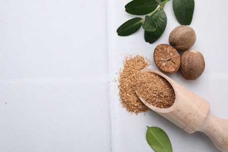 Scoop with gratified nutmeg, seeds and green leaves on white table, flat lay. Space for textの写真素材