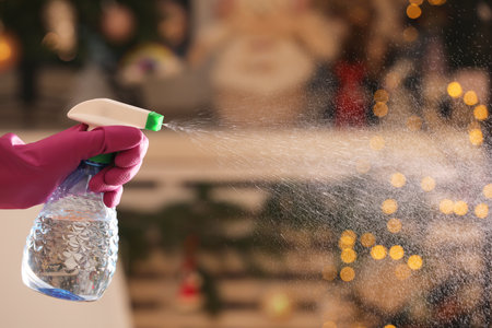 Woman using spray bottle against blurred lights at home, closeup. Space for textの写真素材