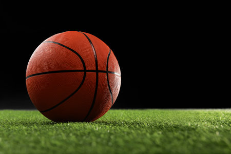 Basketball ball on green grass against black background, space for textの写真素材