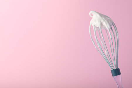 Whisk with whipped egg whites on pink background, space for textの写真素材
