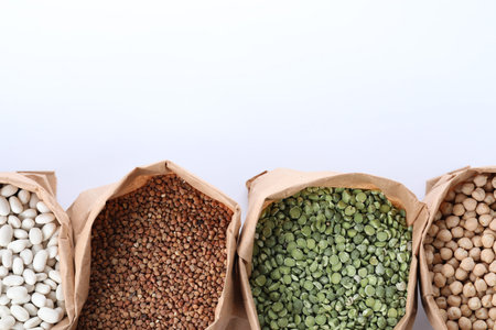 Different types of legumes and cereals in paper bags on white background, top view. Organic grains