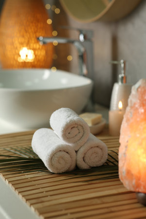 Spa composition. Rolled towels, burning candle and Himalayan salt lamp on countertop in bathroomの写真素材