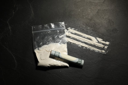 Drug addiction. Plastic bag with cocaine and rolled dollar banknote on gray textured background, flat layの写真素材