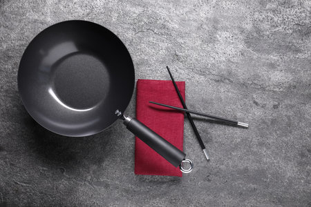 Empty iron wok and chopsticks on gray table, flat layの写真素材