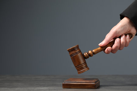 Judge striking mallet at table against gray background, closeup. Space for textの写真素材