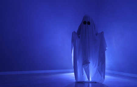Creepy ghost. Woman covered with sheet in blue light, space for text