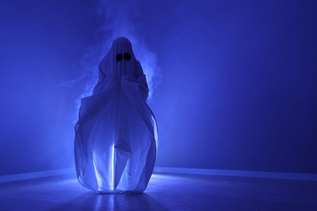 Creepy ghost. Woman covered with sheet in blue light, space for textの写真素材