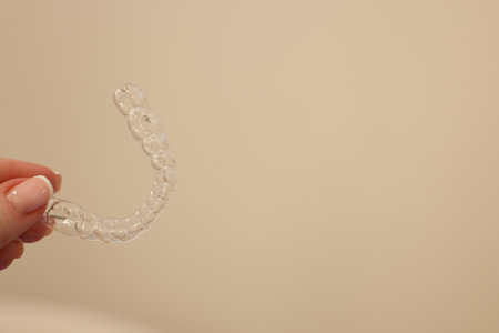Woman with transparent dental aligner on beige background, closeup. Space for text