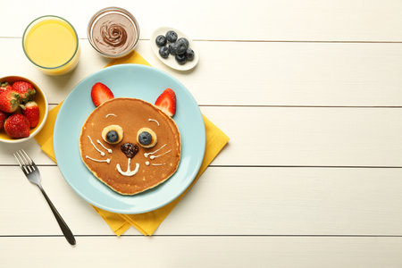 Creative serving for kids. Plate with cute cat made of pancakes, berries, cream, banana and chocolate paste on white wooden table, flat lay. Space for textの写真素材