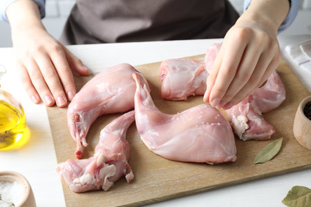 Woman putting salt onto raw rabbit meat at white wooden table, closeupの写真素材