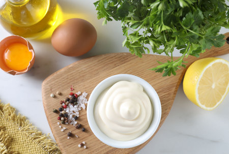 Tasty mayonnaise sauce in bowl, ingredients and spices on white table, flat layの写真素材