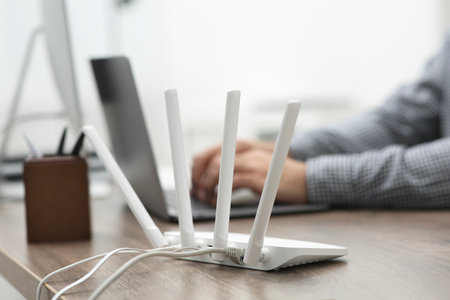 Man with laptop working at wooden table indoors, focus of Wi-Fi router