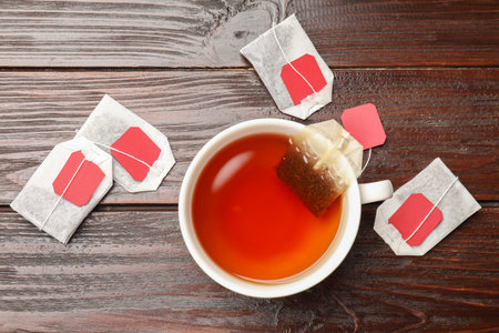 Tea bags and cup of hot beverage on wooden table, flat layの写真素材