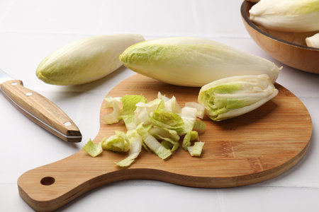 Fresh raw Belgian endives (chicory), wooden board and knife on white tiled table