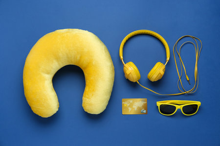 Yellow travel pillow, headphones, sunglasses and credit card on blue background, flat layの写真素材