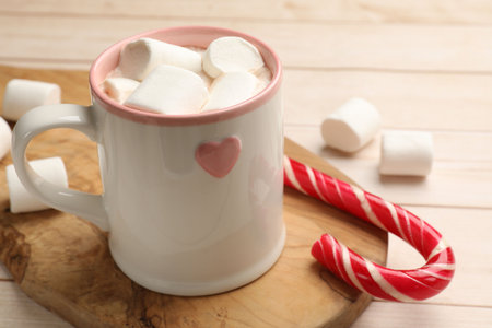 Tasty hot chocolate with marshmallows and candy cane on light wooden table, closeupの写真素材
