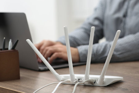 Man with laptop working at wooden table indoors, focus of Wi-Fi router