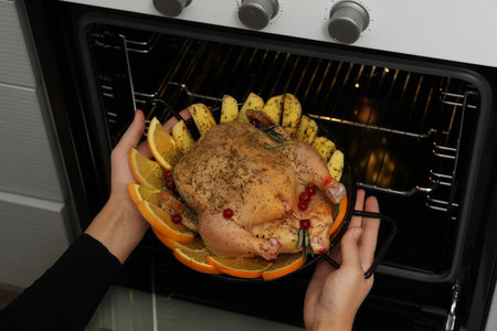 Woman putting chicken with orange and potato slices into oven, closeup