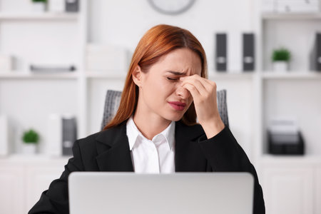 Woman suffering from headache at workplace in officeの写真素材