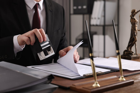 Notary stamping document at table in office, closeup