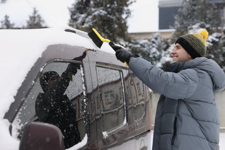 Man cleaning snow from car with brush outdoors
