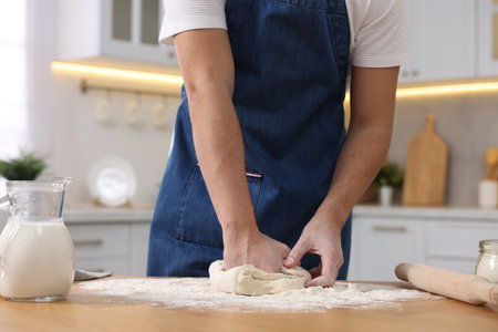 Making bread. Man kneading dough at wooden table in kitchen, closeup