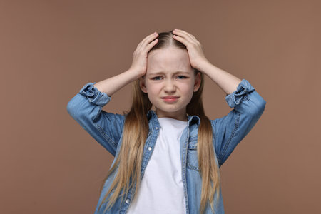 Little girl suffering from headache on brown background