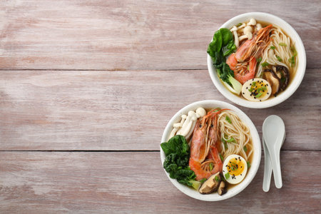 Delicious ramen with shrimps and mushrooms in bowls served on wooden table, flat lay with space for text. Noodle soupの写真素材