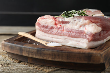 Piece of raw pork belly, salt and rosemary on wooden table, closeupの写真素材
