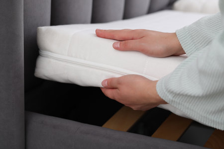 Woman putting new soft mattress on bed, closeup
