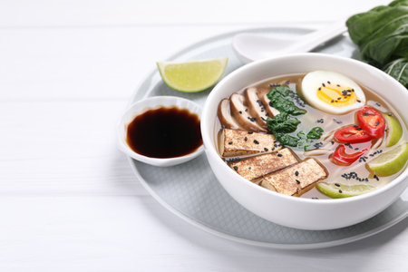 Delicious vegetarian ramen in bowl and soy sauce on white table. Space for textの写真素材