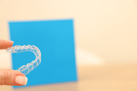 Woman with transparent dental aligner on blurred background, closeup. Space for text