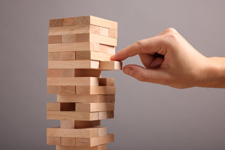 Man removing wooden block from tower on gray background, closeupの写真素材